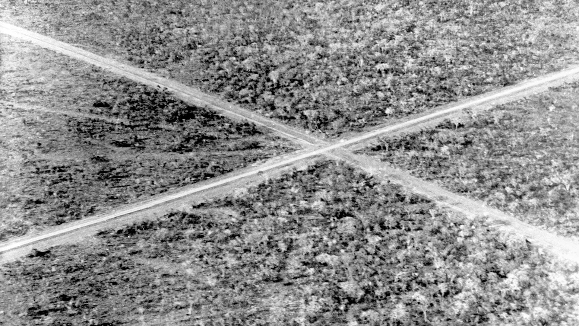 Fotografia de Mário Fontenelle em preto e branco, posicionada ligeiramente à direita da tela, sendo uma estrada de terra bem marcada e batida com um cruzamento no centro.