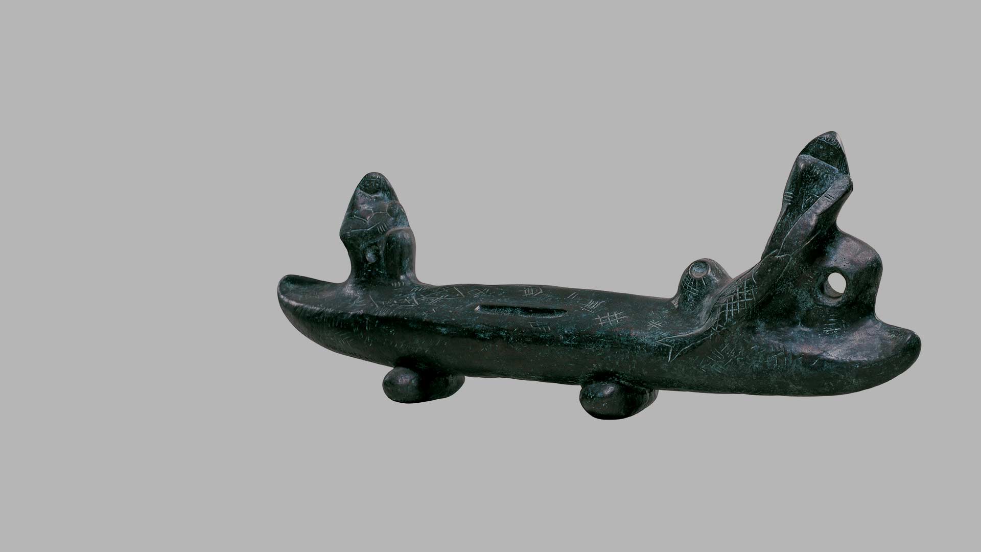 Fotografia de escultura em bronze de Victor Brecheret, denominada “Pirogue” que tem uma temática indígena. Em 3D com formato alongado, uma canoa está apoiada sobre troncos. Na ponta esquerda há uma índia sentada e à direita, um índio segurando um peixe.